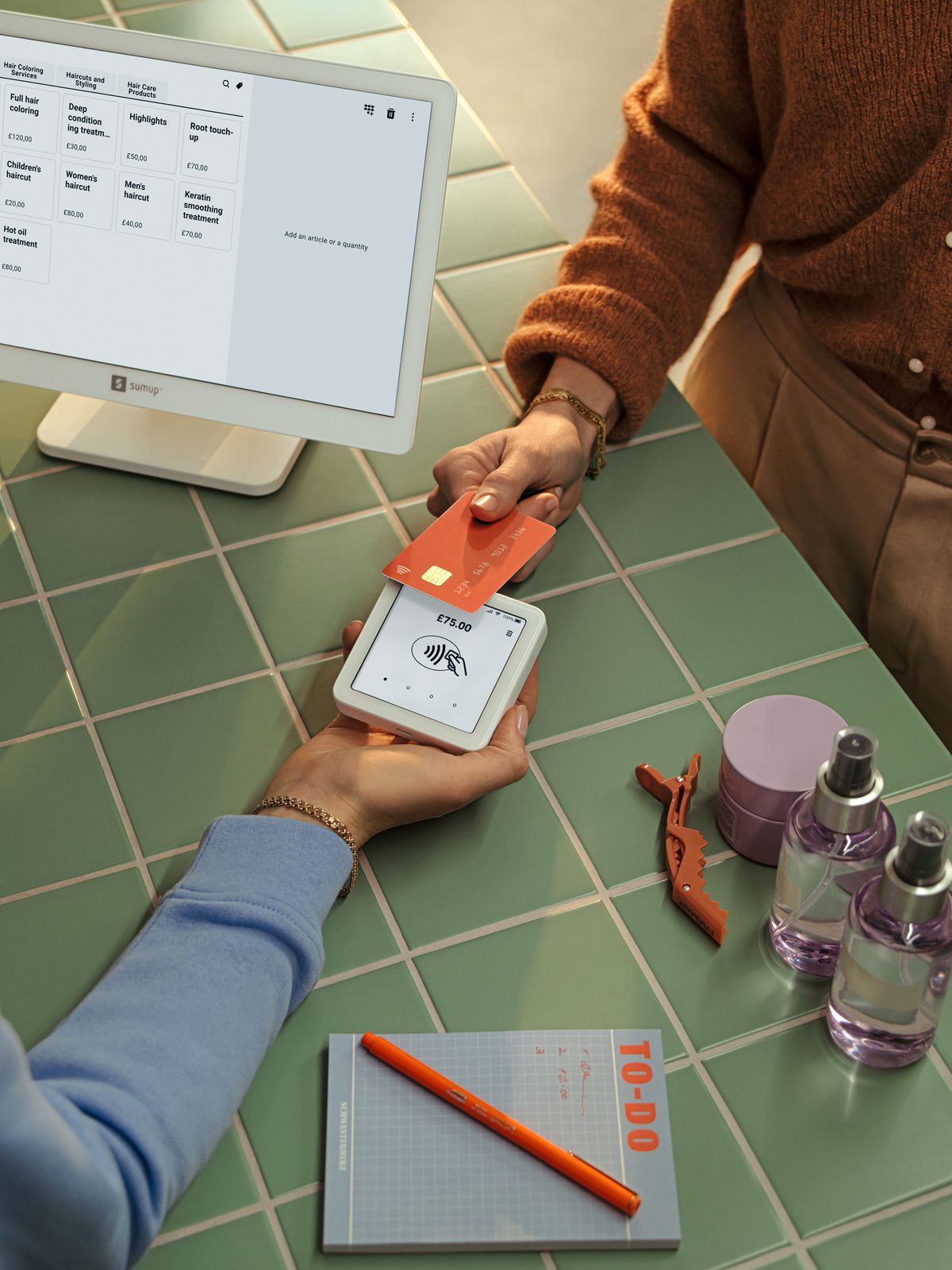 A client paying by card at a salon counter, beside a screen that lists the salon’s services