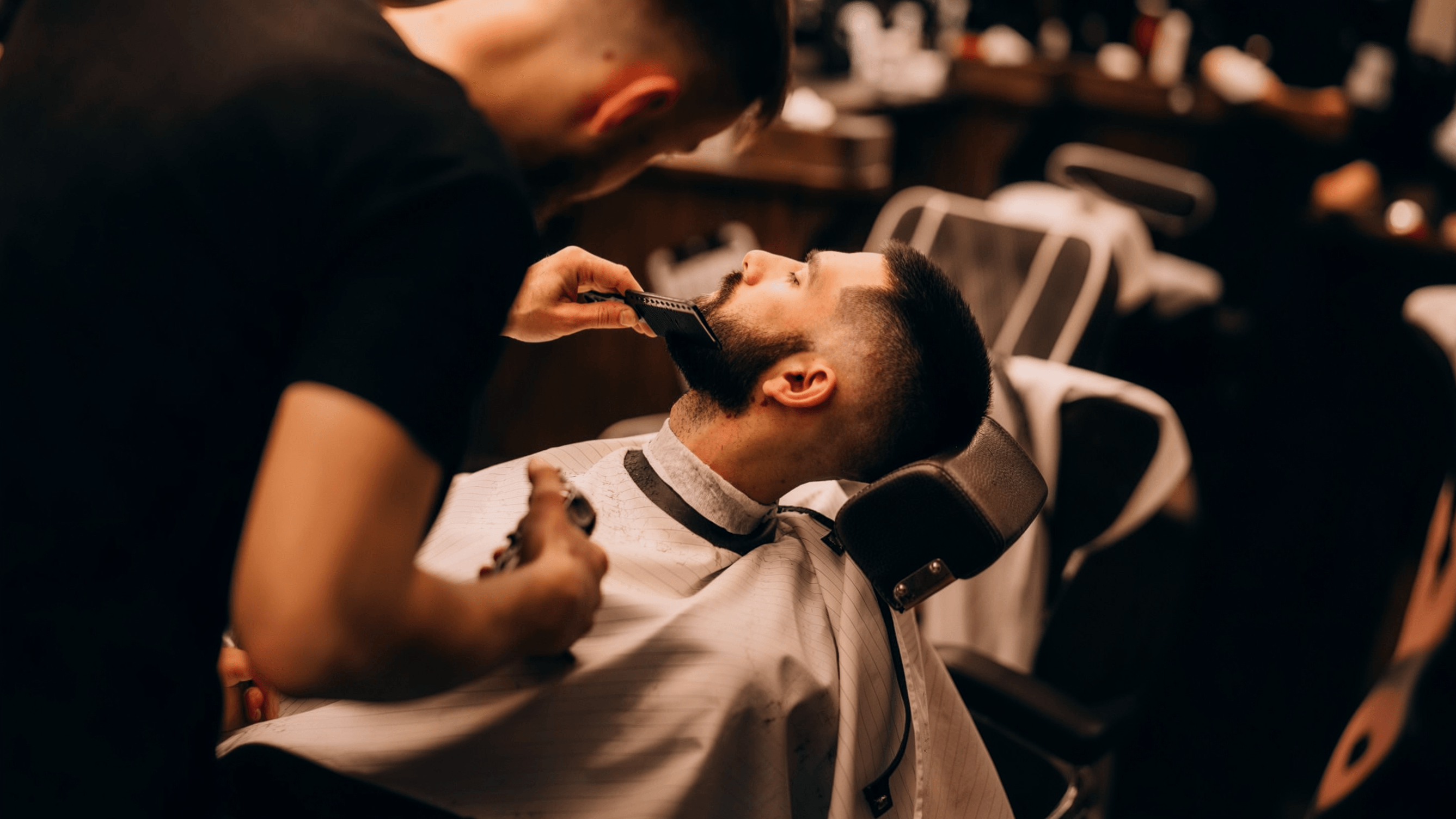 A barber combing a client’s beard in a barbershop